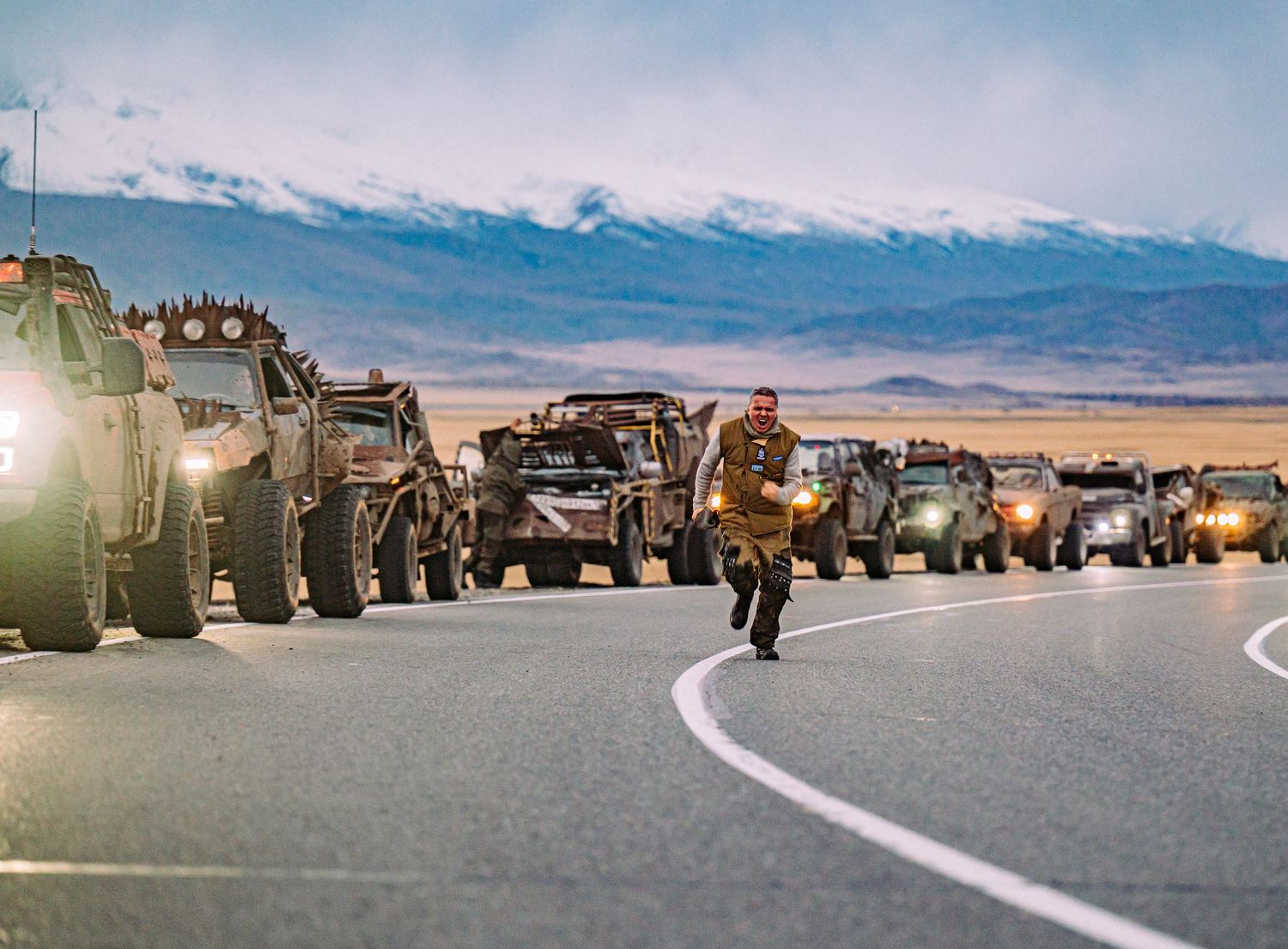 MadWay Rally convoy of Mad Max style vehicles on a mountain road with snowy peaks behind