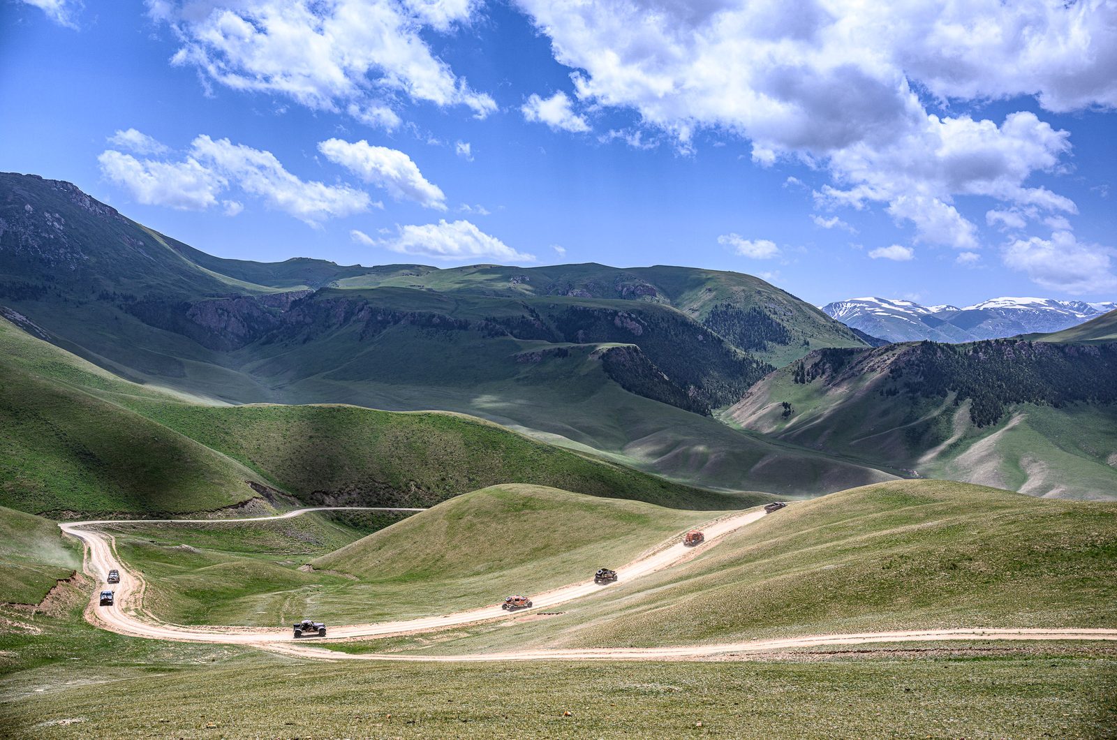MadWay Rally convoy on a winding green mountain road in Kyrgyzstan